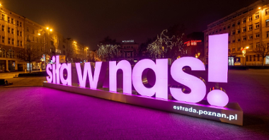 Zdjęcie przedstawia świecący na różowo przestrzenny napis "siła w nas". W tle plac Wolności i budynek Arkadii.