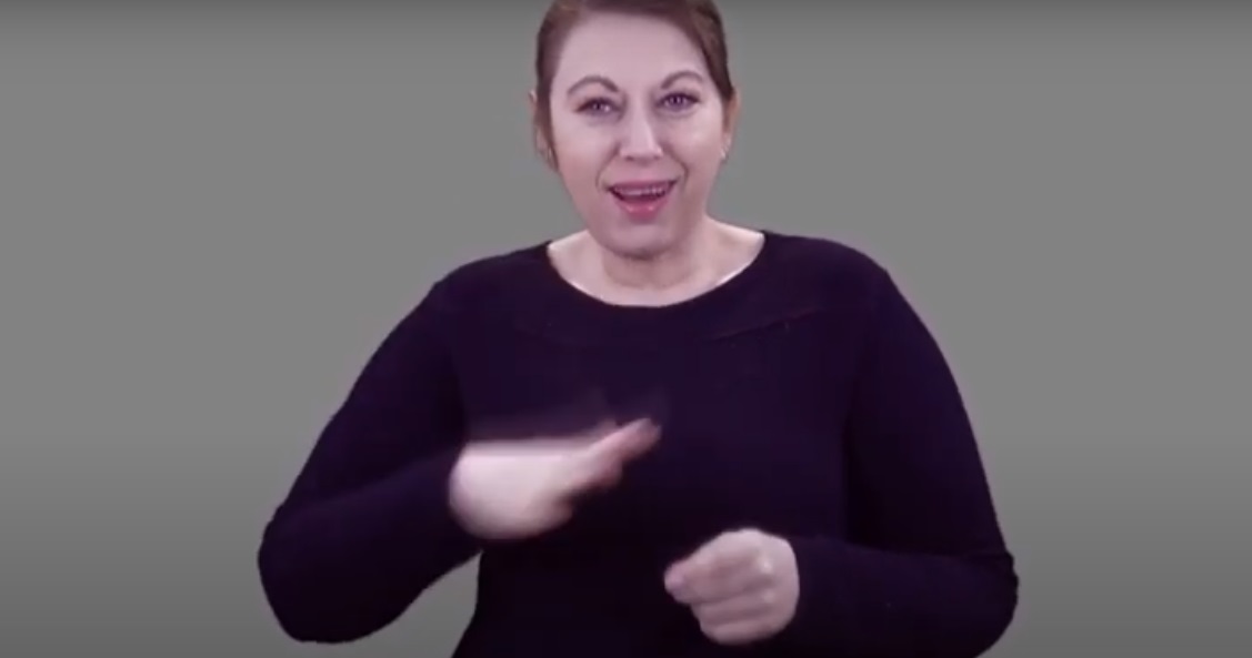 Kadr z filmu: Eunika Lech, tłumaczka polskiego języka migowego, miga, stojąc na szarym tle - grafika artykułu