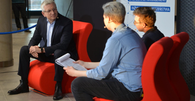 Jacek Jaśkowiak, prezydent Poznania, siedzi na czerwonym krześle, obok dwóch młodych ludzi prowadzi wywiad