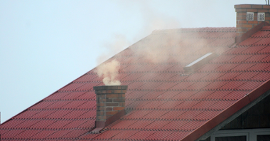 Zdjęcie przedstawia dach z kominem, z którego unosi się dym.