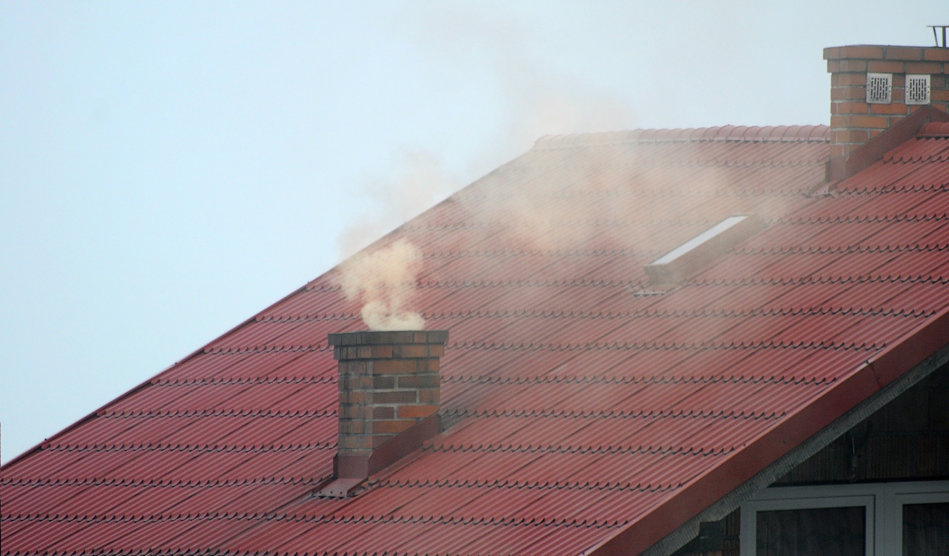 Zdjęcie przedstawia czerwony dach z kominem. Z komina unosi się dym. - grafika artykułu