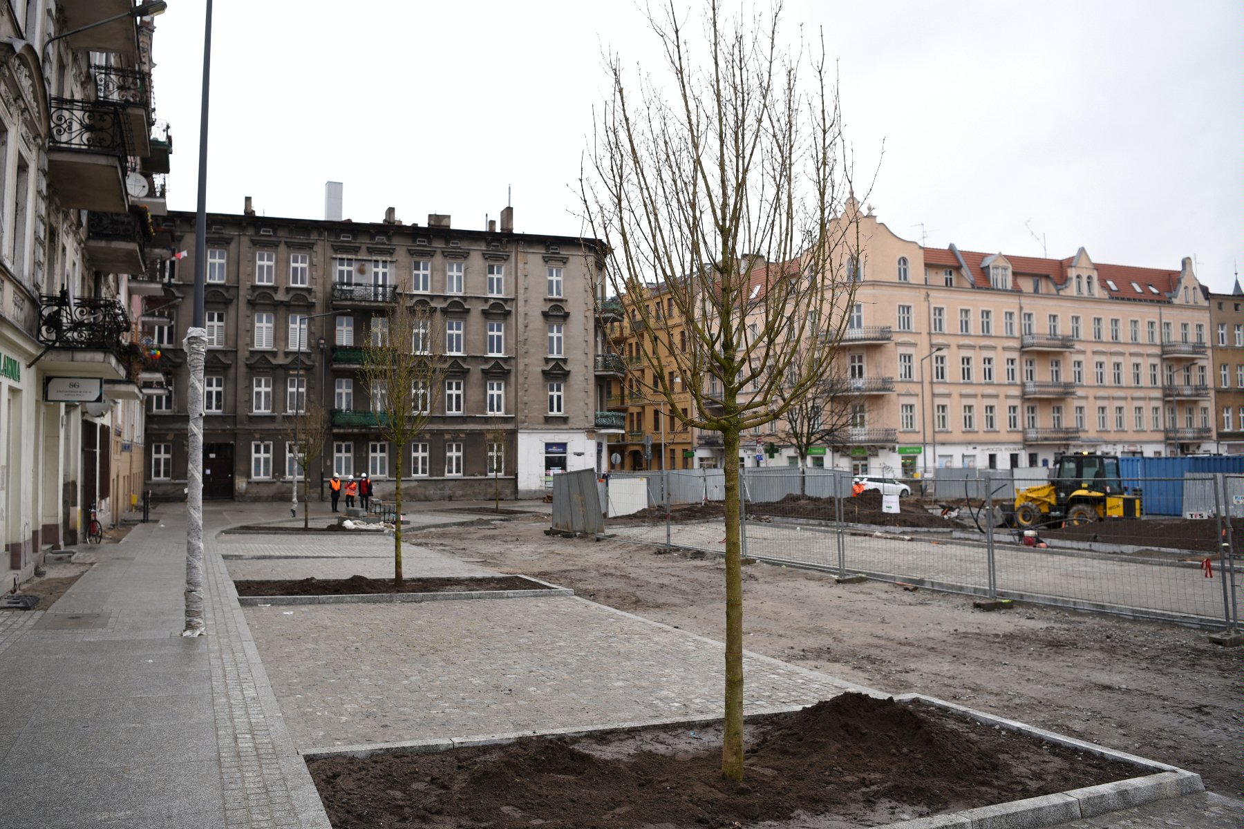 Rynek Łazarski, na pierwszym planie nowe drzewa i przechodnie, w tle plac budowy - grafika artykułu