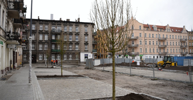Rynek Łazarski, na pierwszym planie nowe drzewa i przechodnie, w tle plac budowy