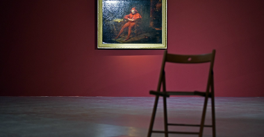 Zdjęcie przedstawia obraz "Stańczyk" autorstwa Jana Matejko. Wisi on w złotej ramie na ścianie. Na pierwszym panie widać krzesło.