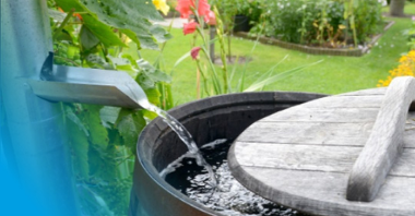 Grafika przedstawia beczkę z wodą w ogrodzie.