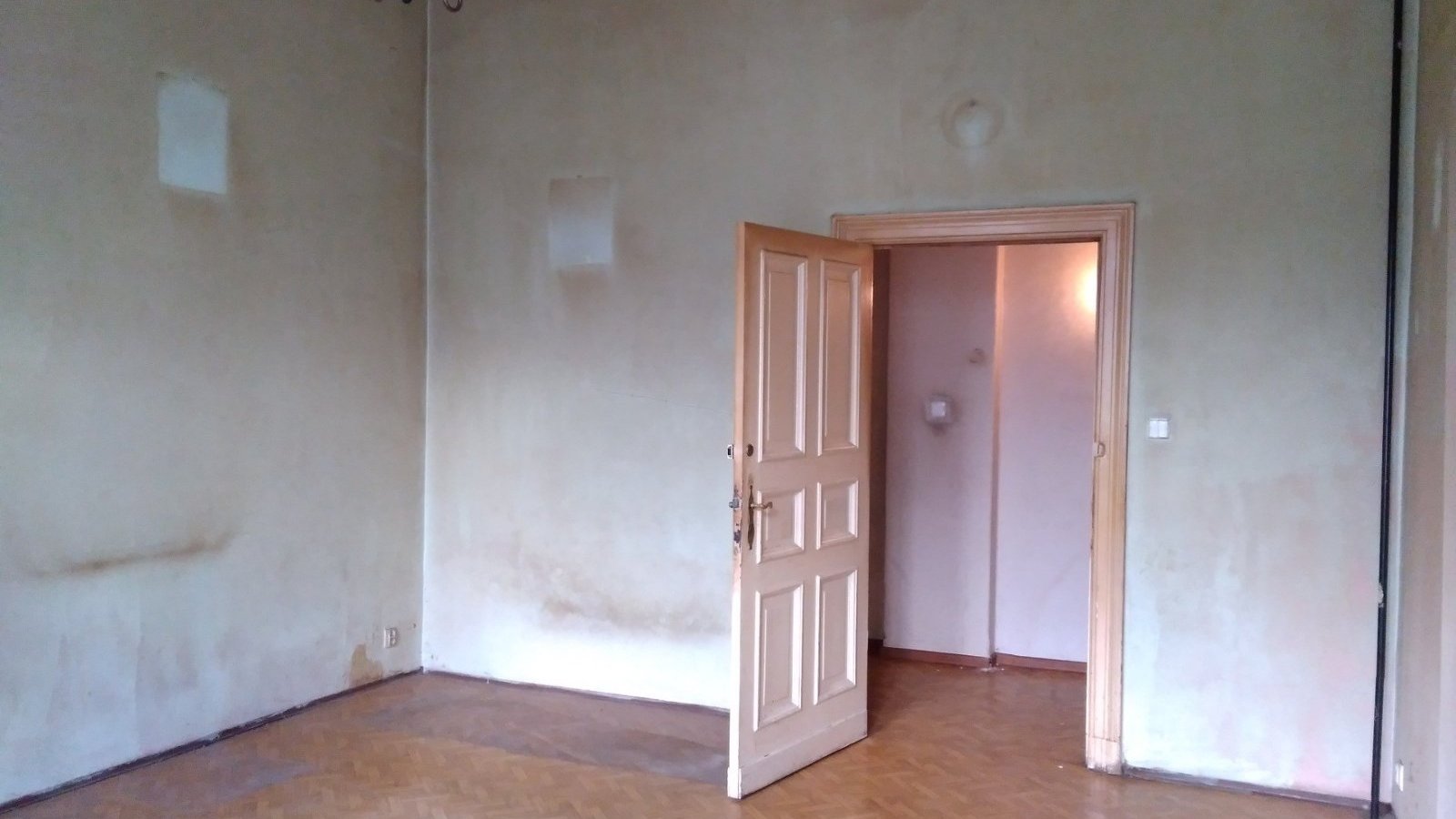 Na zdjęciu duży pokój w kamienicy - do remontu. W centrum duże, otwarte drzwi - grafika artykułu