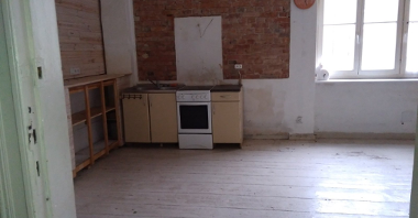 Na zdjęciu pomieszczenie do remontu, w centrum kuchnia, po prawej duże okno