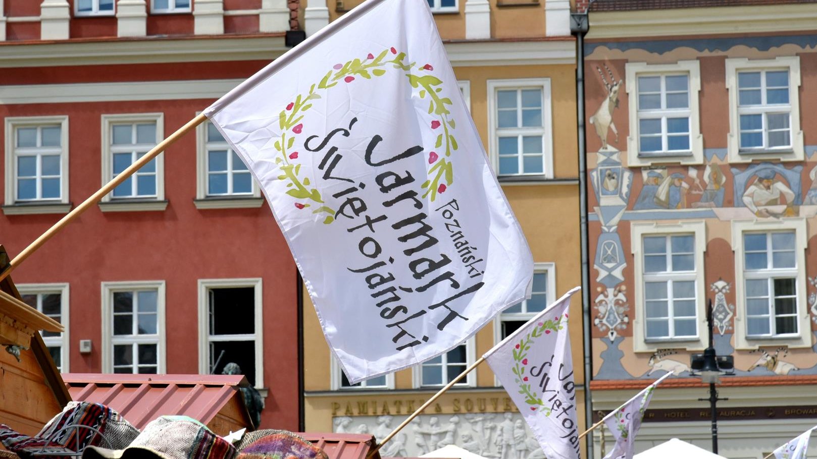 Zdjęcie przedstawia flagi z napisem "Poznański Jarmark Świętojański". - grafika artykułu