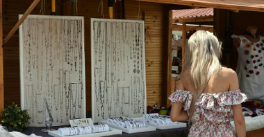 Zdjęcie przedstawia kobietę oglądającą biżuterię sprzedawaną w drewnianym domku.