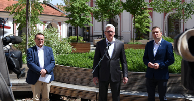Na zdjęciu dziedziniec urzędu miasta, przy mikrofonach stoi trzech mężczyzn, w centrum Jacek Jaśkowiak, obok Mariusz Wiśniewski, w tle drzewa