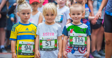 Zdjęcie przedstawia trójkę dzieci, biorących udział w zawodach. Każde z nich ma naklejoną na koszulce naklejkę z imieniem i numerem.