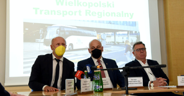 Zdjęcie przedstawia członków zarządu związku siedzących za stołem konferencyjnym. Przed nimi znajdują się mikrofony i woda. W tle znajduje się ekran od rzutnika. Widać na nim autobus oraz napis "Wielkopolski Transport Regionalny".
