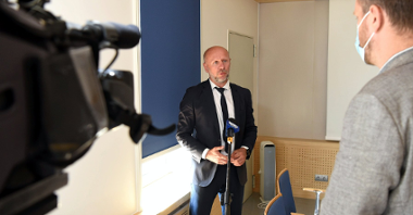 Zdjęcie przedstawia wiceprezydenta Bartosza Gussa rozmawiającego z dziennikarzem. Na zdjęciu widać też kamerę i mikrofon.
