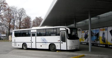 Zdjęcie przedstawia autobus stojący pod wiatą przystankową.