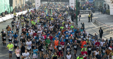Zdjęcie przedstawia biegaczy podczas Poznańskiego Maratonu. Tłum ludzi biegnie ulicami Poznania.