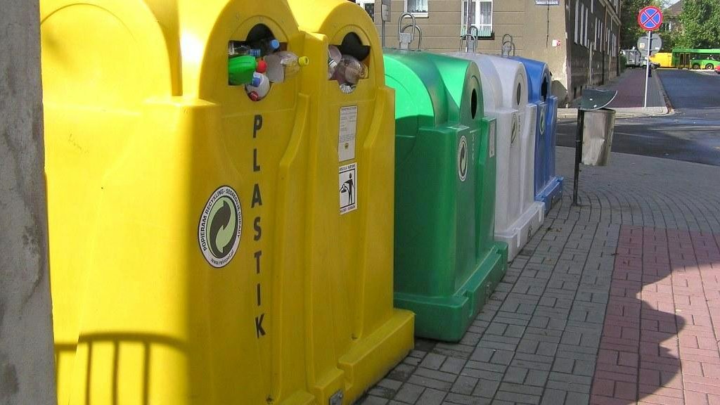 Na zdjęciu cztery kolorowe pojemniki na śmieci stojące obok siebie w rzędzie - grafika artykułu