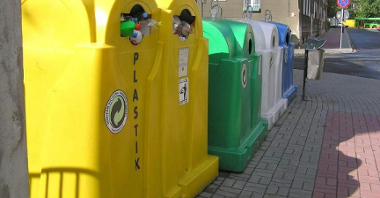 Na zdjęciu cztery różnokolorowe pojemniki na odpady stojące w rzędzie obok siebie