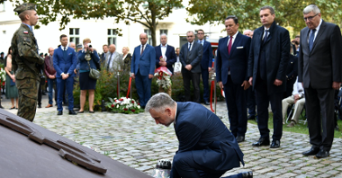 Zdjęcie przedstawia marszałka kładącego znicz pod pomnikiem, za nim stoją przedstawiciele władz samorządowych.
