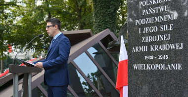 Zdjęcie przedstawia mężczyznę przy mównicy. Na pierwszym planie widać tablicę poświęconą Polskiemu Państwu Podziemnemu.