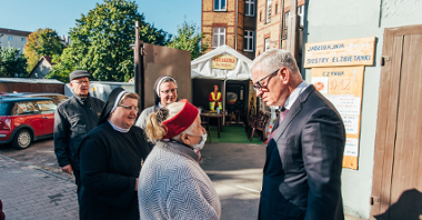 Na zdjęciu Jacek Jaśkowiak, prezydent Poznania, rozmawia ze starszą kobietą w jasnym płaszczu, obok stoją siostry zakonne