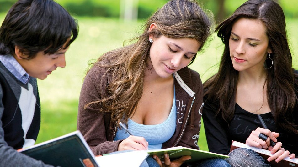 Zdjęcie przedstawia trójkę młodych ludzi - dwie dziewczyny i jednego chłopaka - z zeszytami w ręku, siedzących na trawie. - grafika artykułu