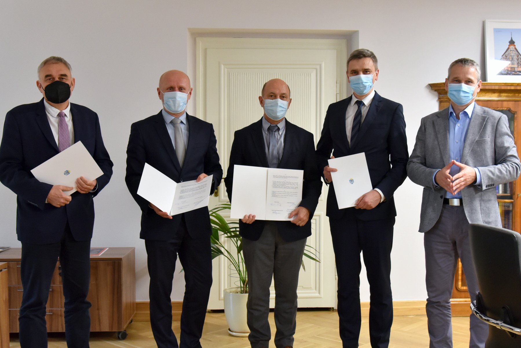 Na zdjęciu pięciu mężczyzn w maseczkach, pozują do zdjęcia, czterech z nich trzyma podpisane porozumienia - grafika artykułu