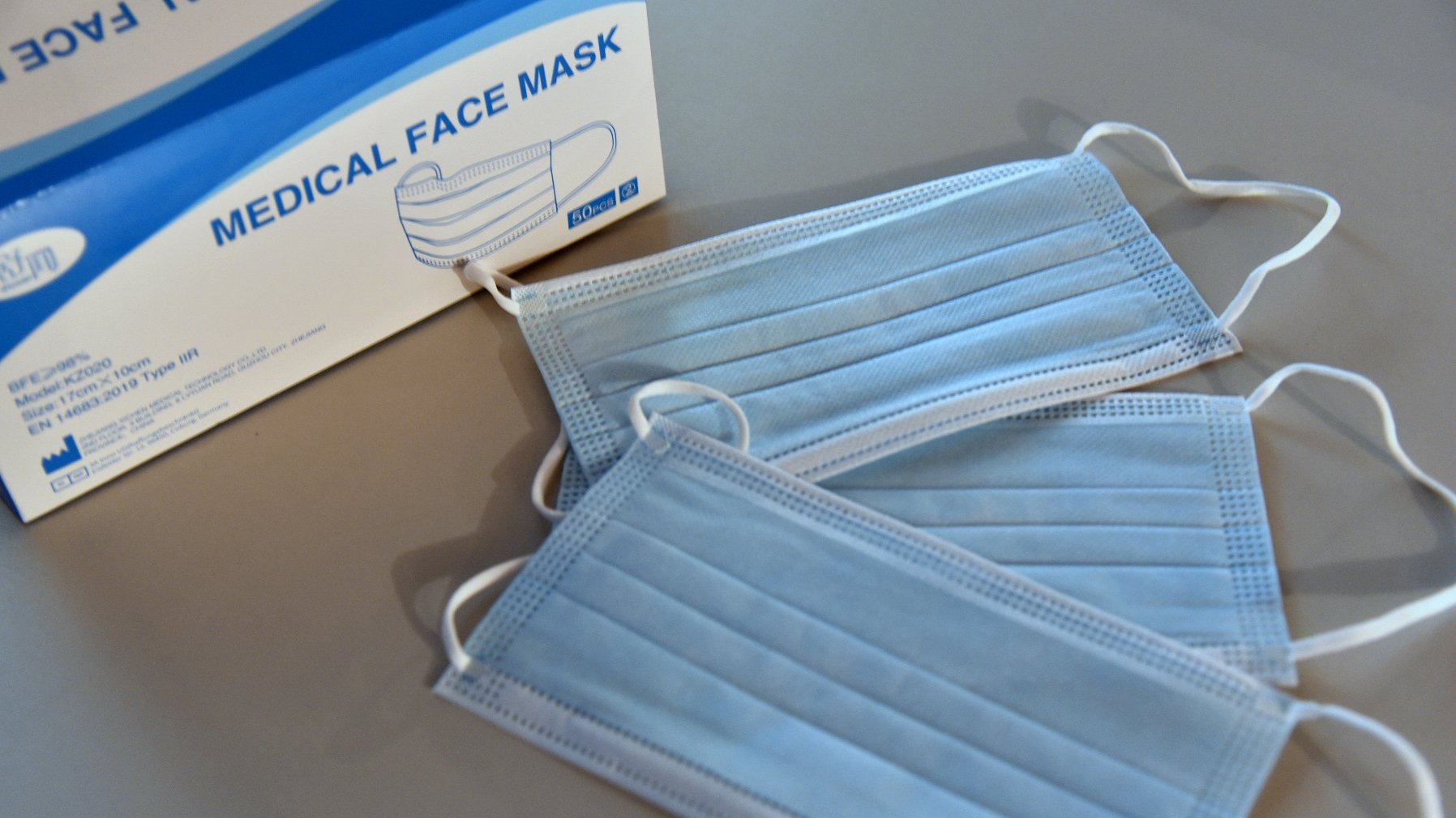 Trzy maseczki leżące obok siebie, w pobliżu pudełko z napisem: medical face mask