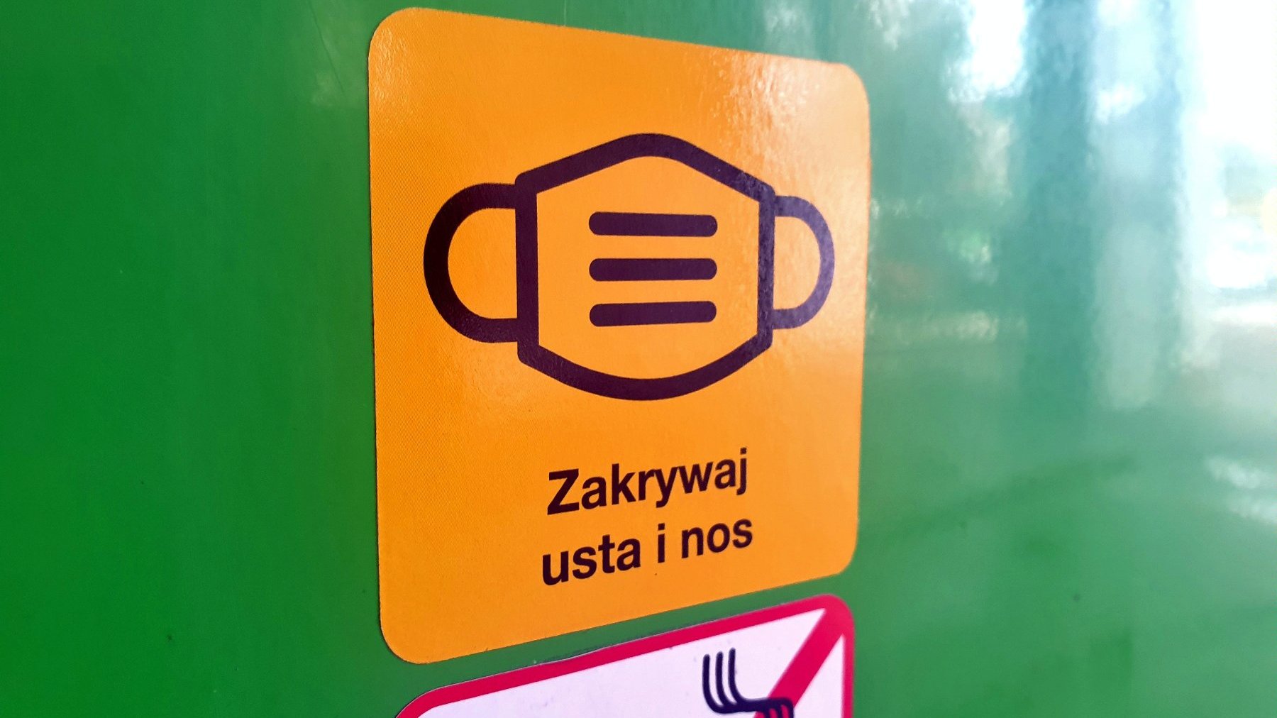 Naklejony na tramwaj piktogram: maseczka, pod nią napis: zakrywaj usta i nos