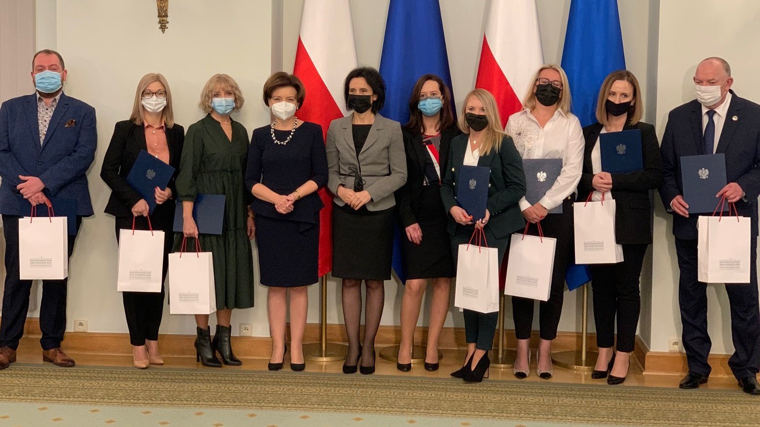Zdjęcie przedstawia osoby nagrodzone stojące na tle flag Polski i Unii Europejskiej. - grafika artykułu