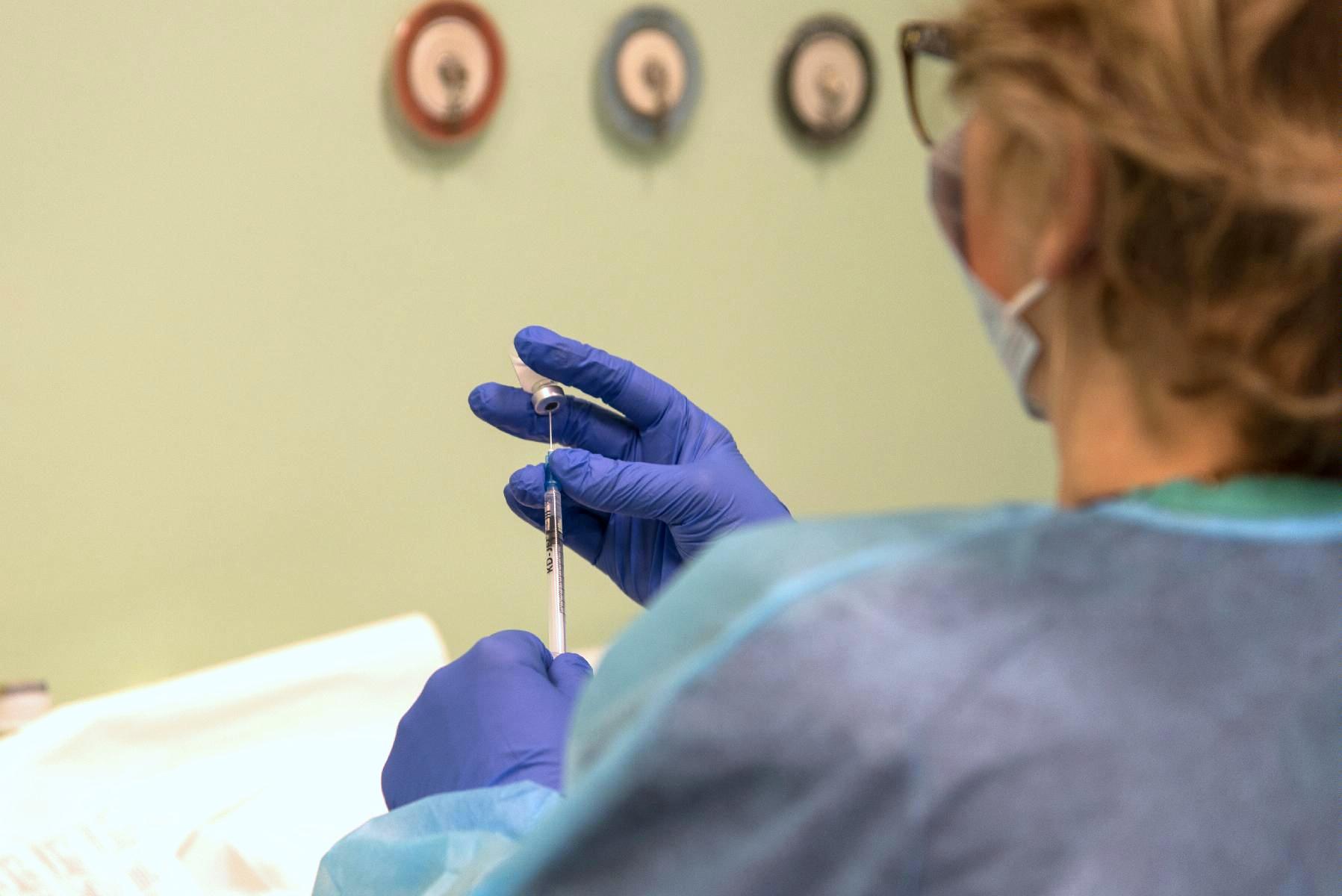 Na zdjęciu kobieta przygotowująca szczepionkę, w centrum jej dłonie i strzykawka - grafika artykułu