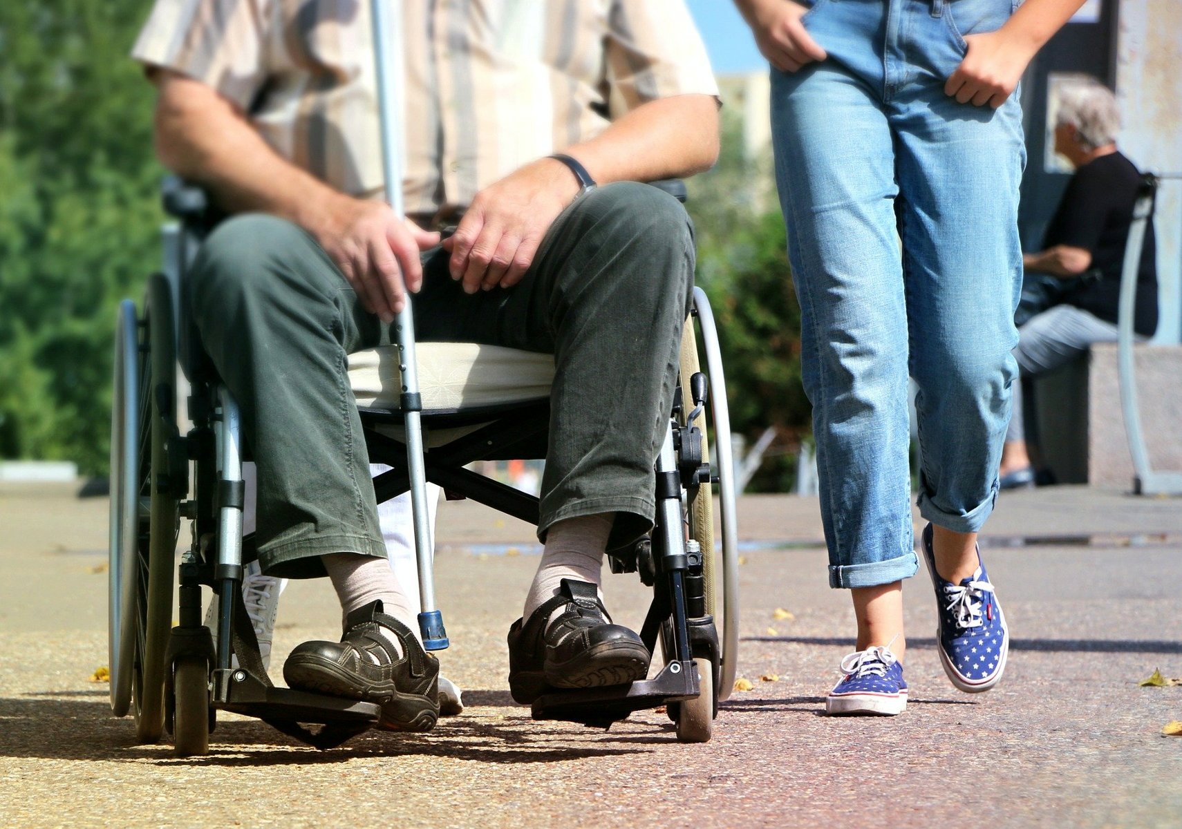 Zdjęcie przedstawia dwie osoby, jedna z nich znajduje się na wózku inwalidzkim. Na fotografii jest zbliżenie na nogi. - grafika artykułu