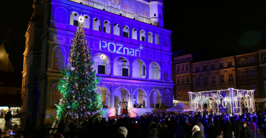 Zdjęcie przedstawia oświetlony na niebiesko Ratusz. Obok niego stoi choinka. Na zdjęciu widać też tłum ludzi oraz świąteczne iluminacje.