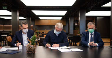 Zdjęcie przedstawia trzech mężczyzn za stołem. W środku znajduje się prezydent Poznania podpisujący umowę.