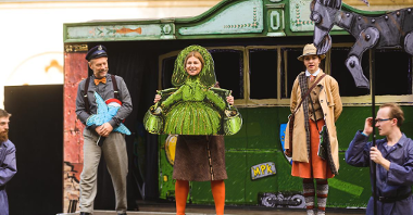 Zdjęcie przedstawia aktorów na scenie. Jedna z kobiet jest przebrana za Bamberkę, jeden z mężczyzn za maszynistę. Są też dekoracje - koziołek i tramwaj.