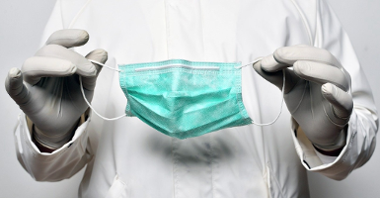 Zdjęcie ilustracyjne: osoba w medycznym fartuchu trzymająca maseczkę
