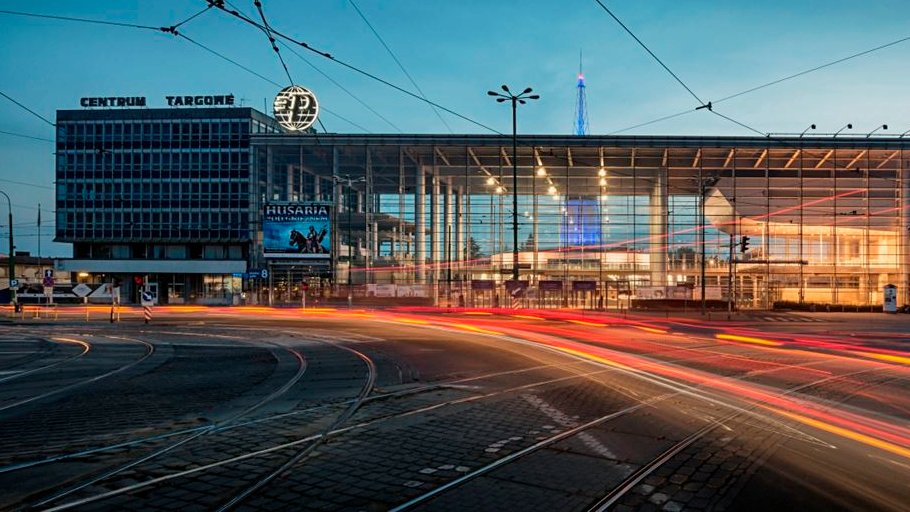 Na zdjęciu wejście główne na Międzynarodowe Targi Poznańskie, na pierwszym planie ślady świateł samochodów - grafika artykułu
