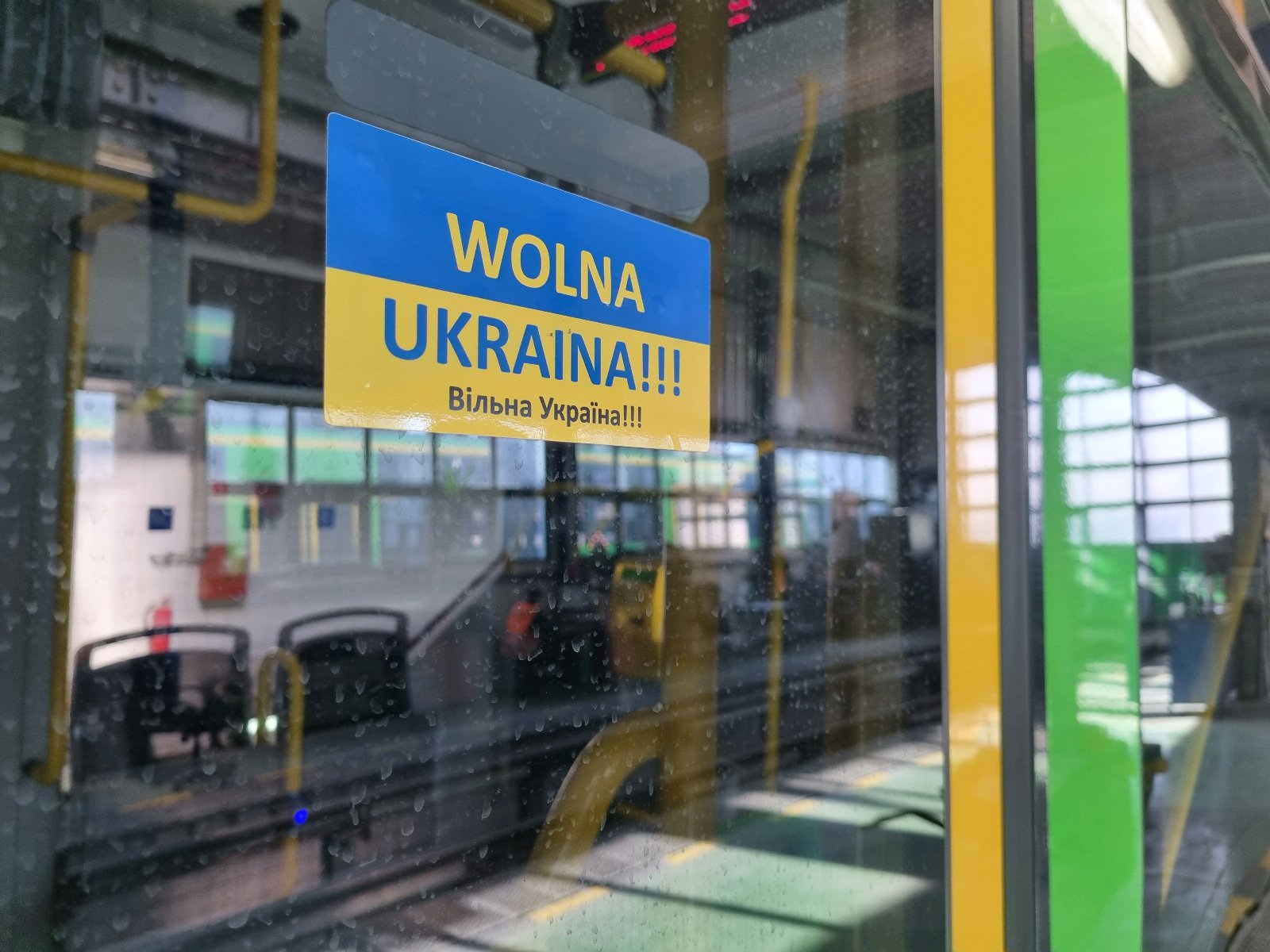 Niebiesko-żółta naklejka z napisem Wolna Ukraina po polsku i ukraińsku naklejona na drzwiach tramwaju - grafika artykułu