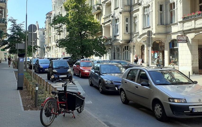 Na zdjęciu poznańska ulica, na niej samochody, na pierwszym planie chodnik i zaparkowany na nim rower - grafika artykułu