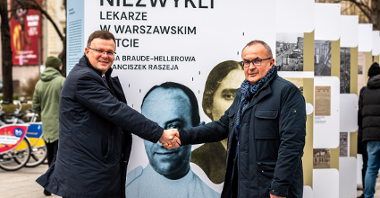 Na zdjęciu dwóch mężczyzn podających sobie dłonie na tle wystawy