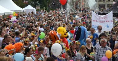 Na zdjęciu tłum uśmiechniętych ludzi, starszych, dorosłych i dzieci, niektórzy trzymają balony; nad nimi bańki mydlane