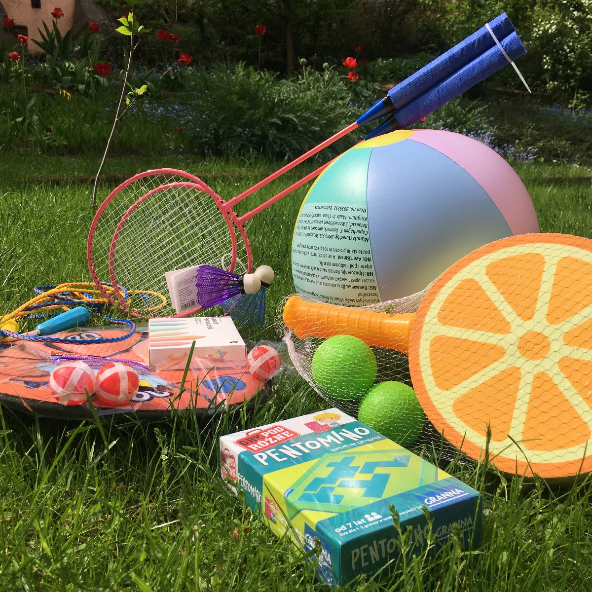 Na zdjęciu zestaw leżących na trawie zabawek, wśród nich piłka, paletki, lotki i gra planszowa - grafika artykułu