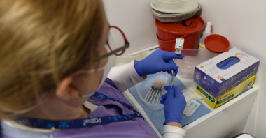 Na zdjęciu kobieta przygotowująca szczepionkę, obok leżą strzykawki i pudełko medycznych rękawiczek
