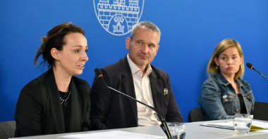 Na zdjęciu trzy osoby za stołem konferencyjnym, dwie kobiety, jedna z nich mówi do mikrofonu oraz jeden mężczyzna