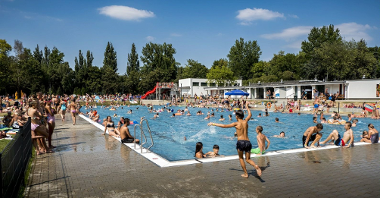 Zdjęcie przedstawia tłumy ludzi na pływalni letniej w parku.