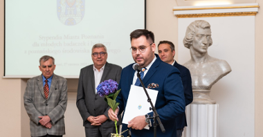 Na zdjęciu stypendysta przy mikrofonie, za nim zastępca prezydenta Poznania, przewodniczący rady miasta i przewodniczący kapituły