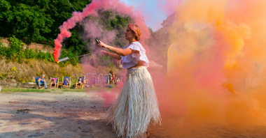 Zdjęcie przedstawia kobietę puszczającą kolorowy dym.