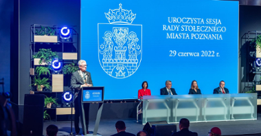 Na zdjęciu prezydent Poznania przy mównicy, obok przewodniczący i wiceprzewodniczący rady miasta, w tle ekran z herbem miasta