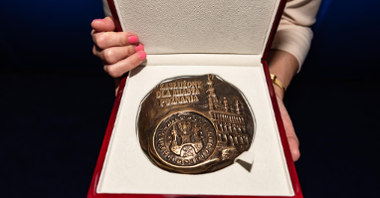 Na zdjęciu medal z napisem: zasłużony dla miasta Poznania, trzymany przez kobiece dłonie