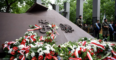 Na zdjęciu pomnik, pod nim wiązanki biało-czerwonych kwiatów