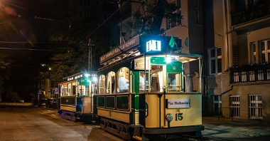 Na zdjęciu zabytkowy tramwaj stojący na torach, oświetlony lampami, po zmierzchu
